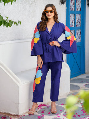 Part of the Heavenly Hues collection, this statement top is a masterpiece adorned with meticulously crafted fabric appliqué flowers, delicately framed by intricate zardosi borders. The floral motifs are elevated with exquisite cutwork detailing that adds depth, texture, and sophistication. Designed with a contemporary notch lapel and elegant bell sleeves, the silhouette blends timeless craftsmanship with modern refinement. A celebration of floral artistry and graceful design.