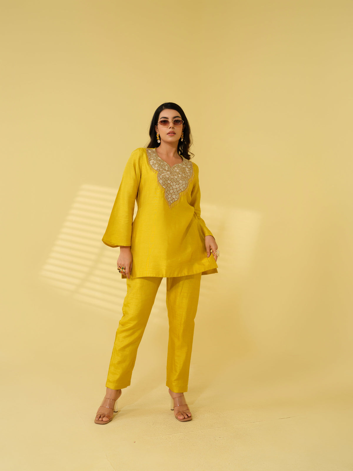 Step into effortless elegance with these luxurious co-ord sets, available in radiant marigold yellow and deep crimson red. The co -ord set features a meticulously embellished neckline, combining the precision of zari machine embroidery with the charm of delicate handwork detailing, creating a rich and intricate design that exudes traditional artistry. The flared sleeves and straight-cut silhouette add a graceful, contemporary touch, while the coordinated pants offer a clean, polished finish.